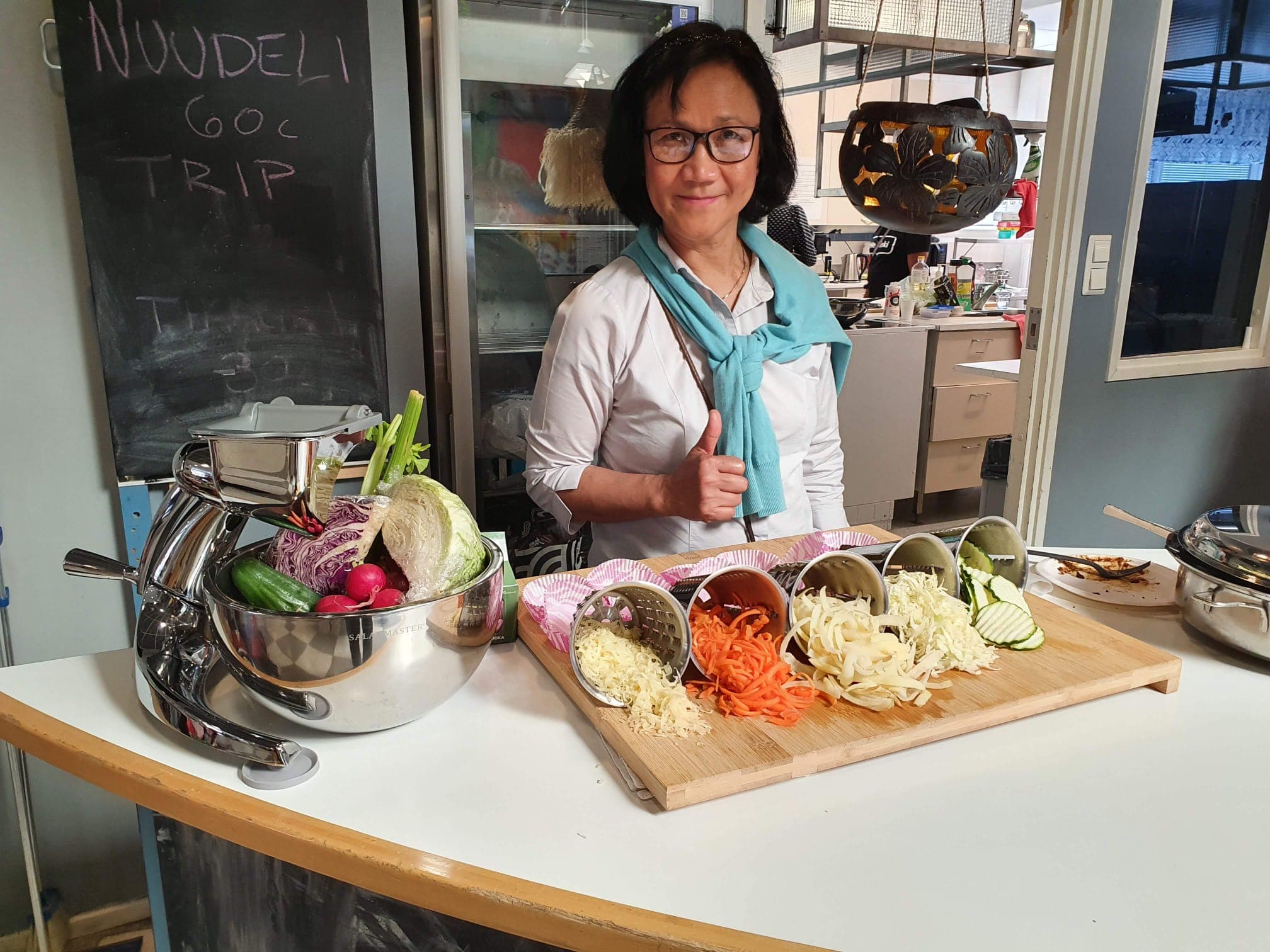 Cynthia at a cooking show with the food processor and a board of freshly shredded vegetables